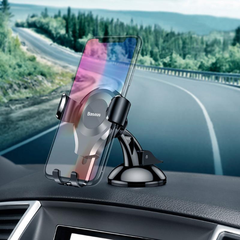 Baseus dashboard-mounted phone holder in use on a car's center console, holding a smartphone securely while driving.